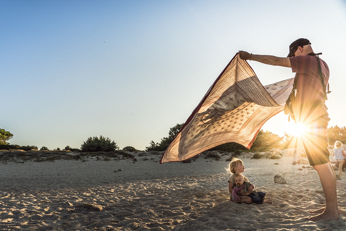 LIFEforFIVE-Pack-System-Papa Daniel bei Sonnenuntergang am Strand. Schüttelt ein Tuch über zwei seiner Töchter aus.