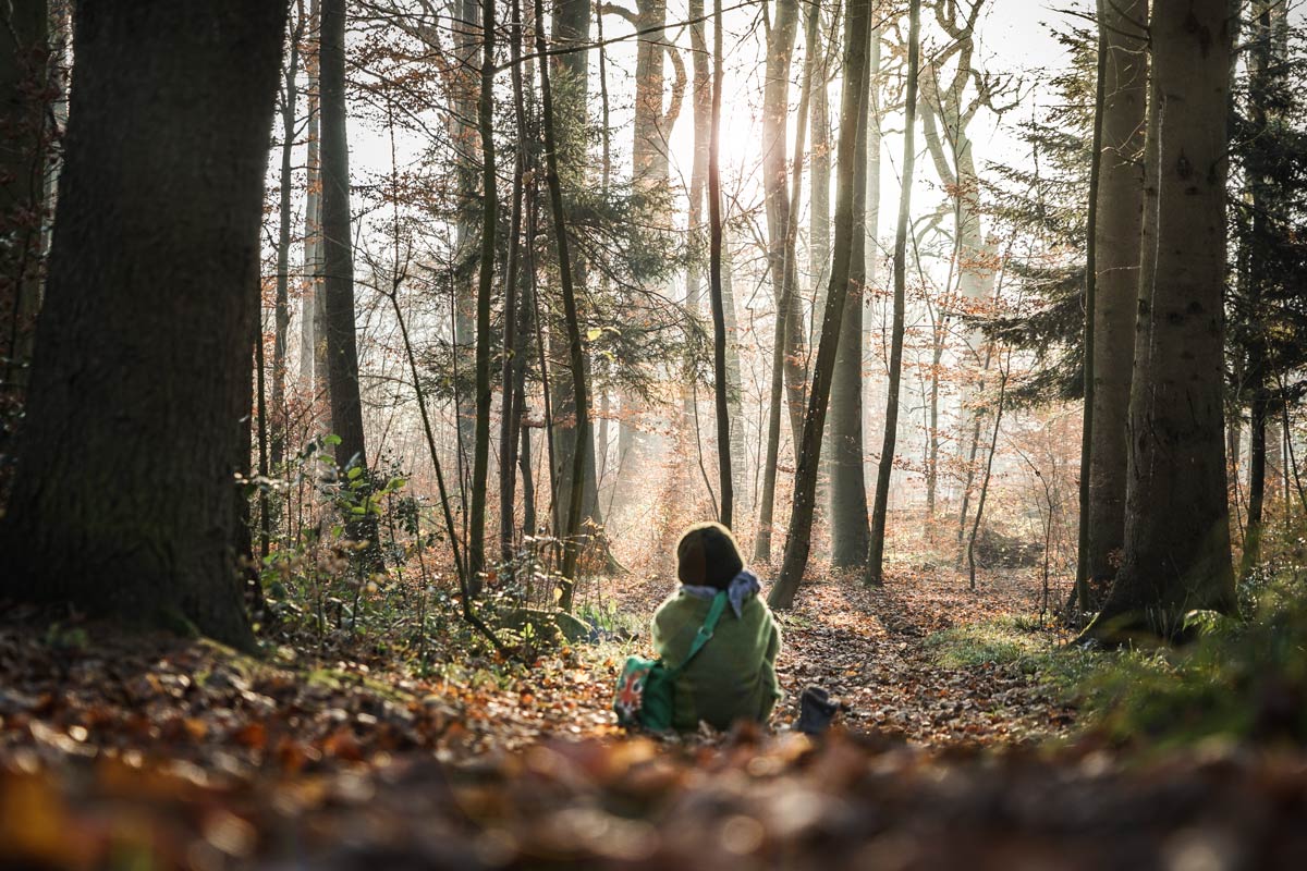 LIFEforFIVE-Suedamerika- Mädchen sitzt in Wollkleidung am Boden im Herbstwald